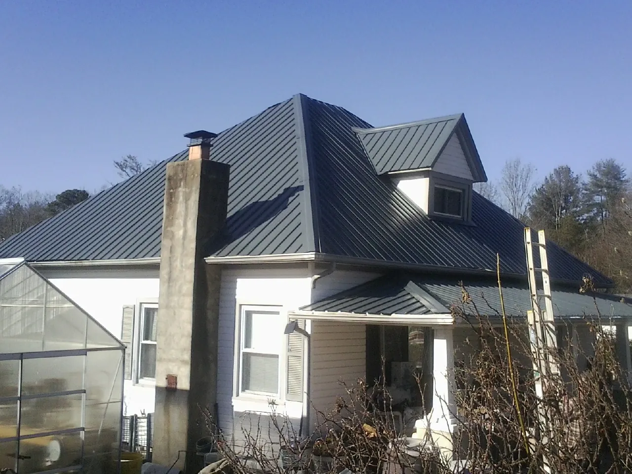 Dark blue standing seam metal roof on a white farmhouse with dormer — Slate & Tile Roof Repair by Roofing Brothers in Hays
