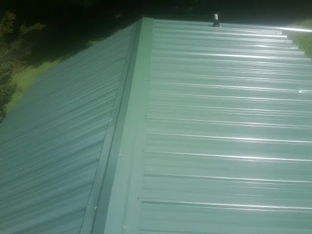 New green metal panels meeting at the ridge of a roof — Flat Roof Repair work by our crew in Hays