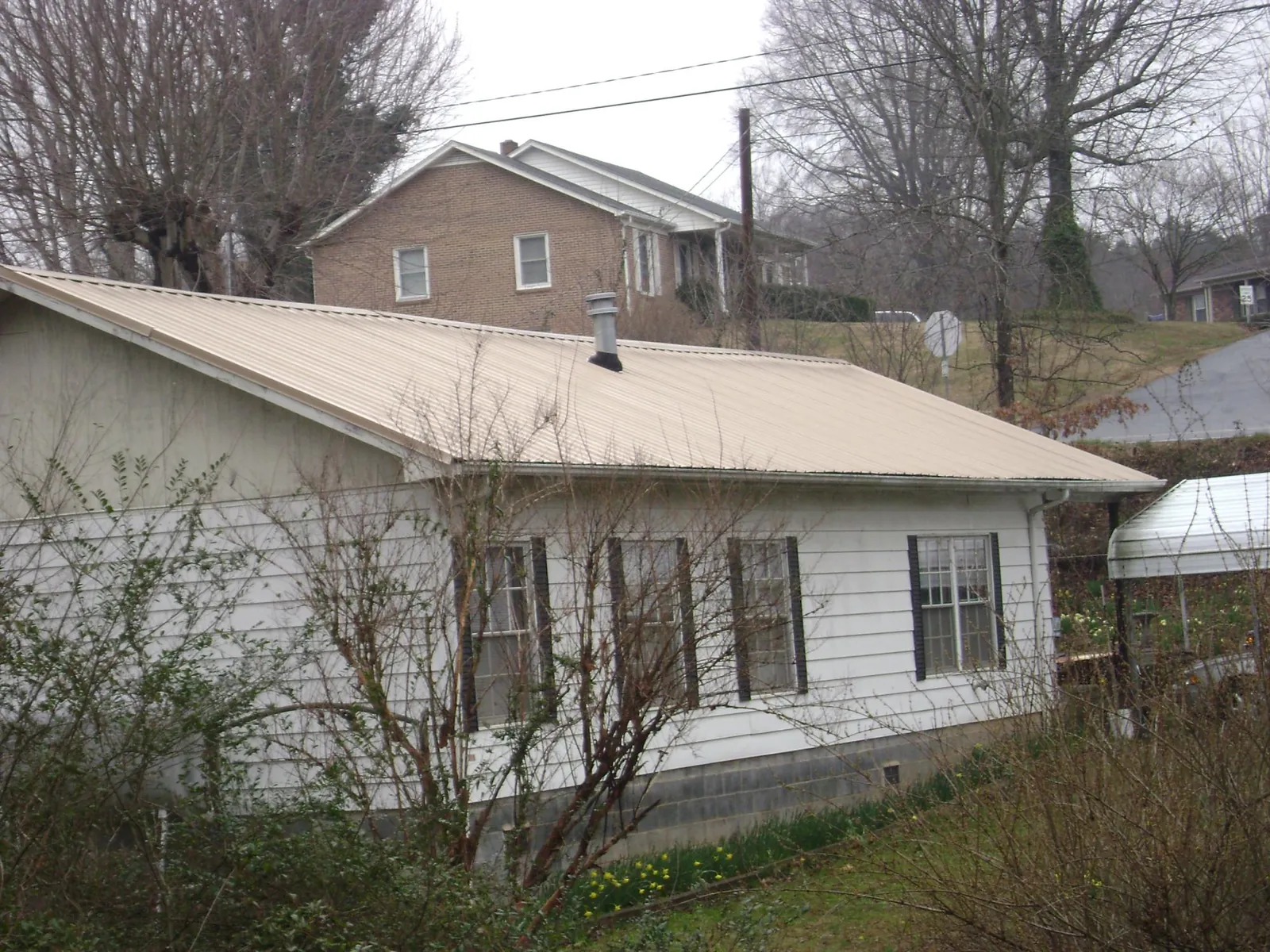 Tan metal roof on a white sided house set into a hillside — Commercial Roofing by Roofing Brothers in Hays